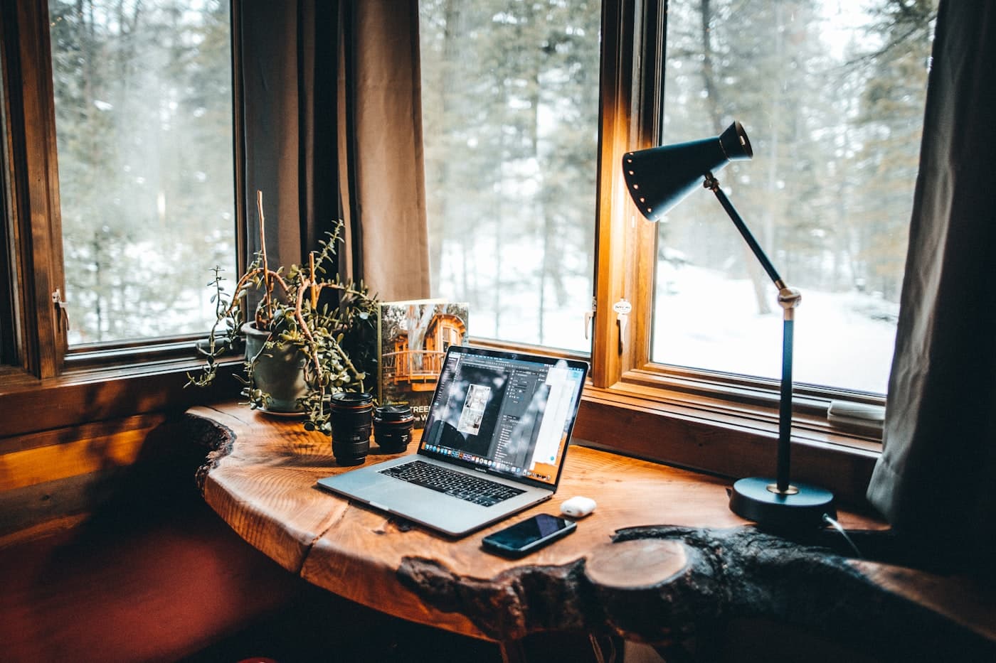 A warm wood desk by a forest window, laptop open